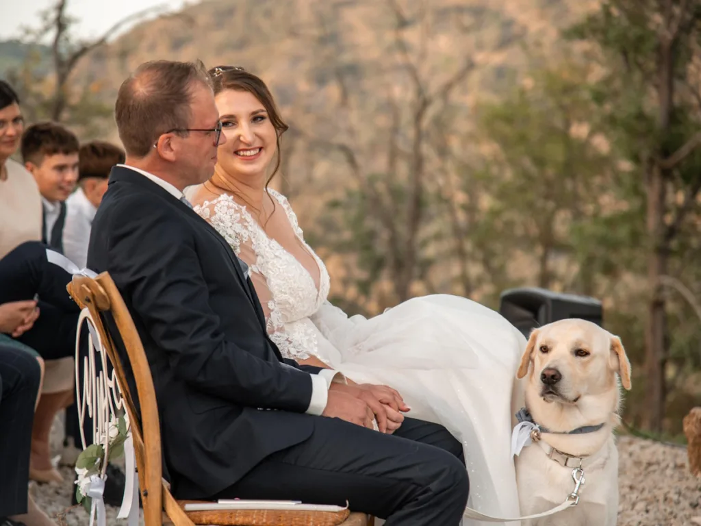 Das Hochzeitspaar lächelt sich an und der Hund sitzt dabei.